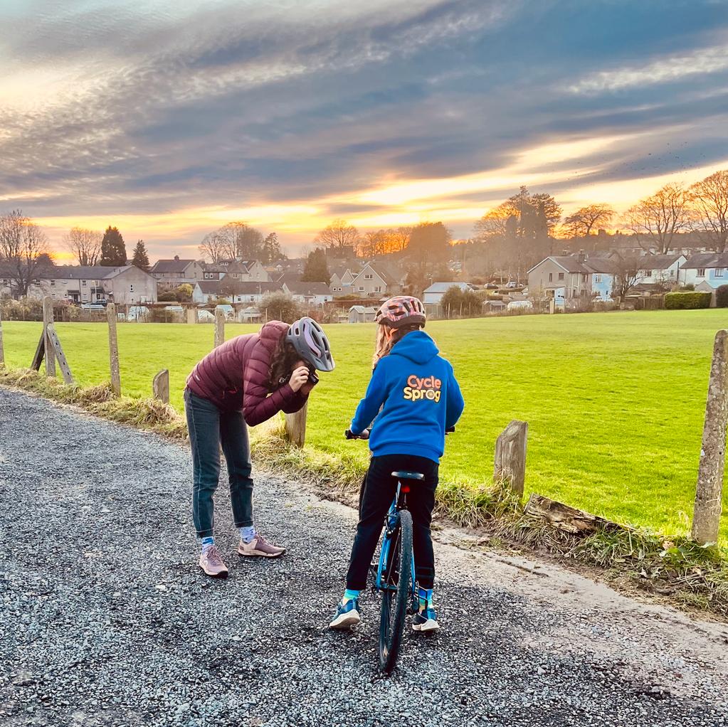 woman in a pink jacket taking a photo of a girl on a bike