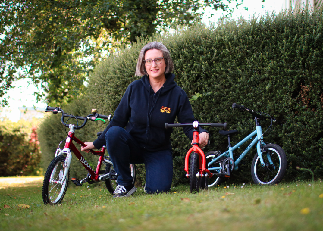 Karen Gee, founder of Cycle Sprog kneeling on the grass with three kids bikes