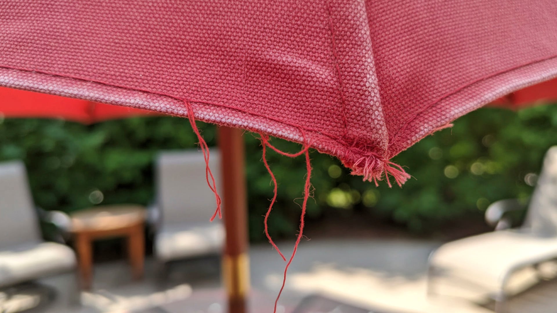 Close-up of a damaged California Umbrella patio umbrella canopy with loose threads and fraying along the seam.