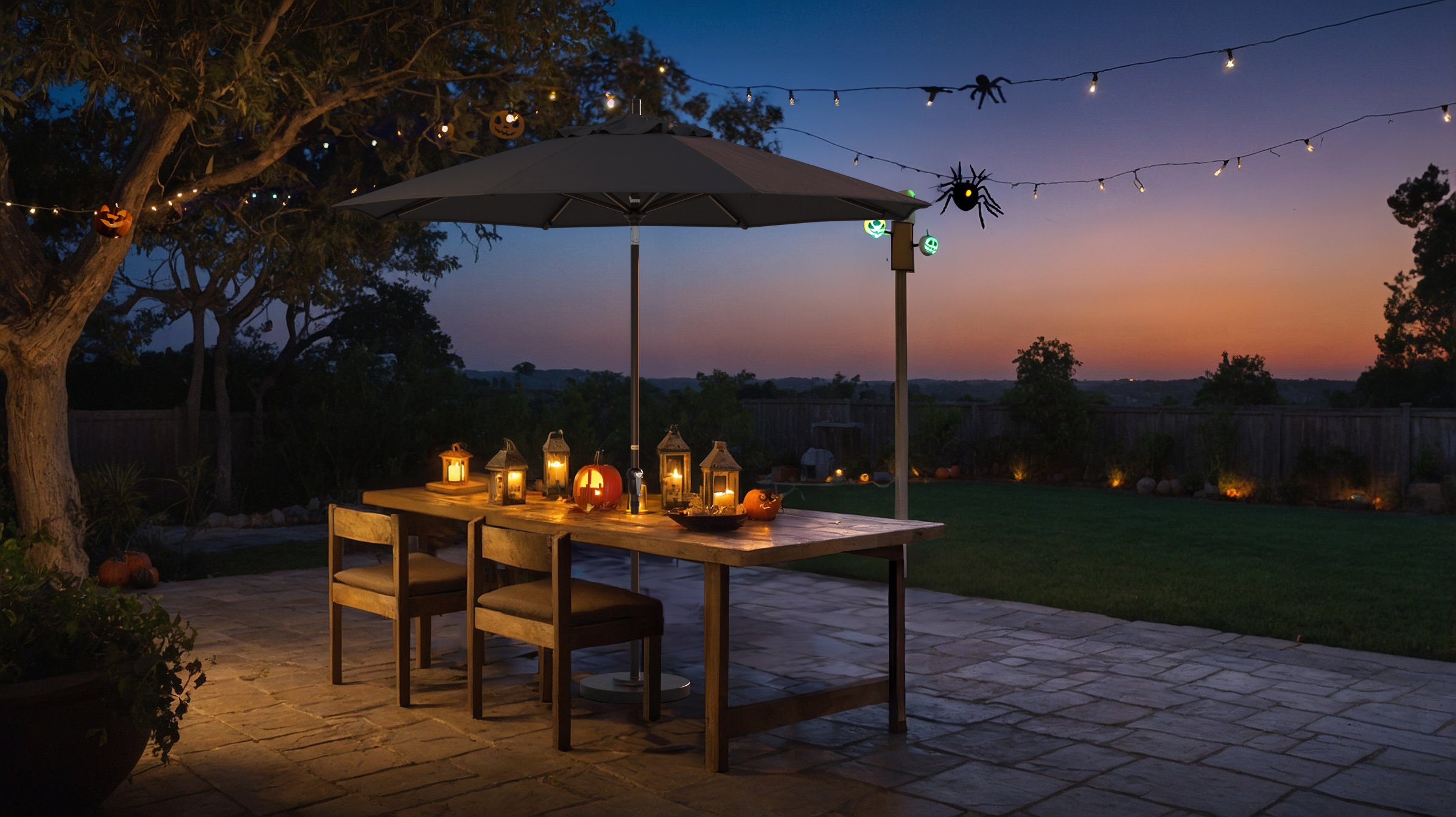 Spooky outdoor Halloween setup featuring a California Umbrella Sunset Series with Sunbrella fabric, casting a warm glow over a patio table adorned with jack-o'-lanterns, lanterns, and Halloween-themed string lights at dusk.