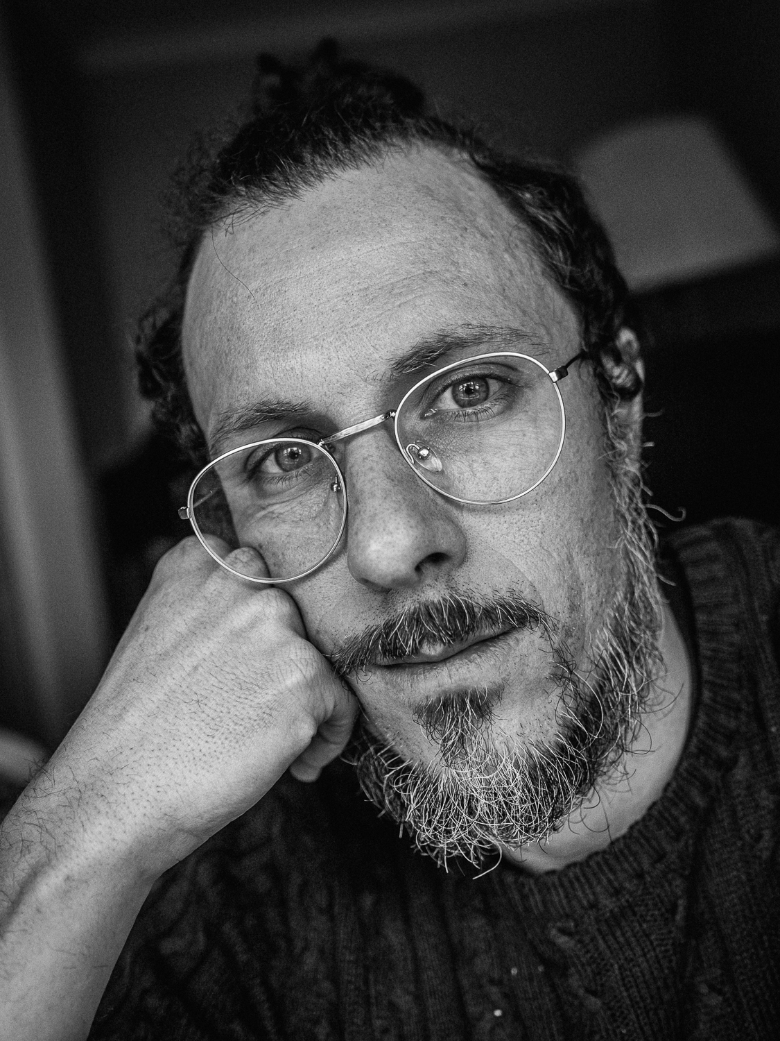 Black and white photo of a man with glasses and a scrappy beard, leaning on a loosely-clenched fist. He looks tired.
