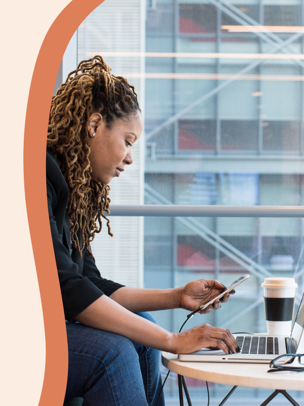 Woman with braids working on her phone with laptop in front - dream catch consulting
