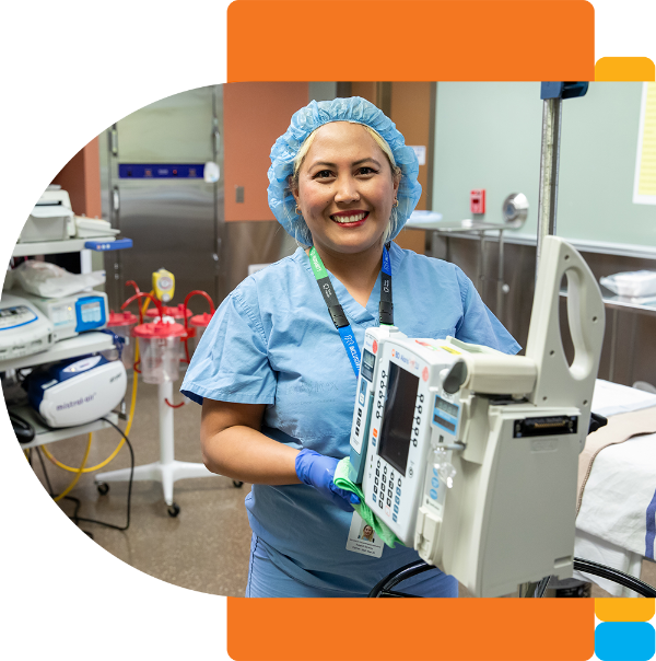 A housekeeping attendant wearing blue scrubs, gloves and a hair net is wiping down a piece of medical equipment