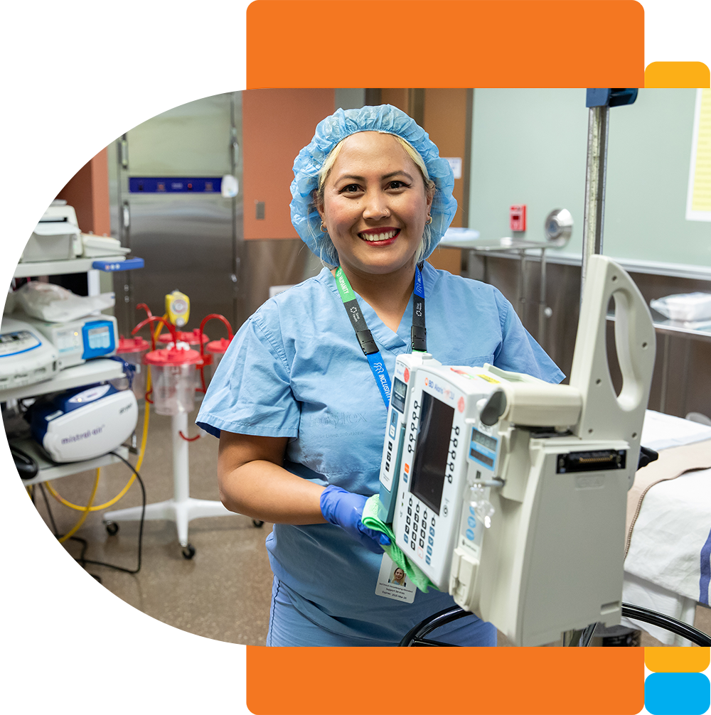 A housekeeping attendand in blue scrubs and gloves is smiling while cleaning a medical device