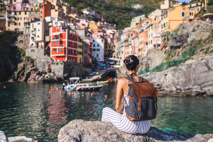 Young tourist relaxing by the sea, looking at the beautiful town Riomaggiore, Cinque Terre, Liguria
