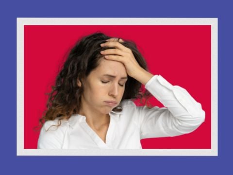 White female with dark curly hair wearing a white shirt with her eyes closed and hand on forehead sighing