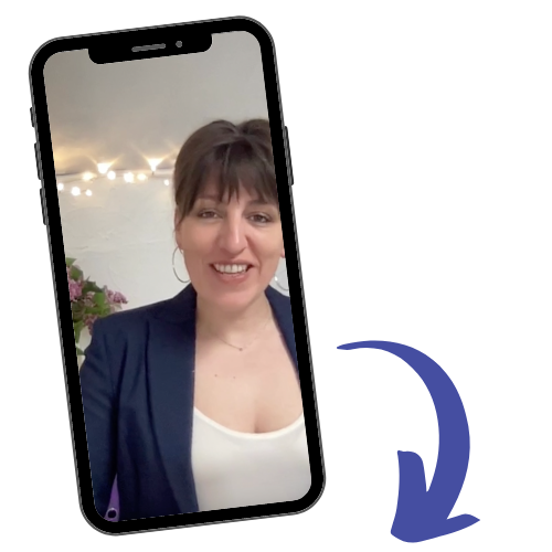 Image of Sophie viewed on a mobile phone. Female with dark hair smiling wearing large hoop earings, a navy jacket and scoop neck white top with a fine necklace. In the background are fairy lights on the ceiling and the edge of some flowers.