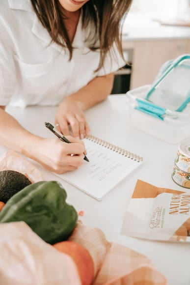 Person writing a gluten free meal plan surrounded by fresh produce and gluten free pantry items