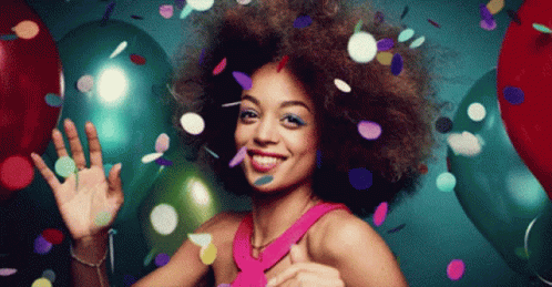 Beautiful girl with afro hair dances surrounded by confetti and balloons