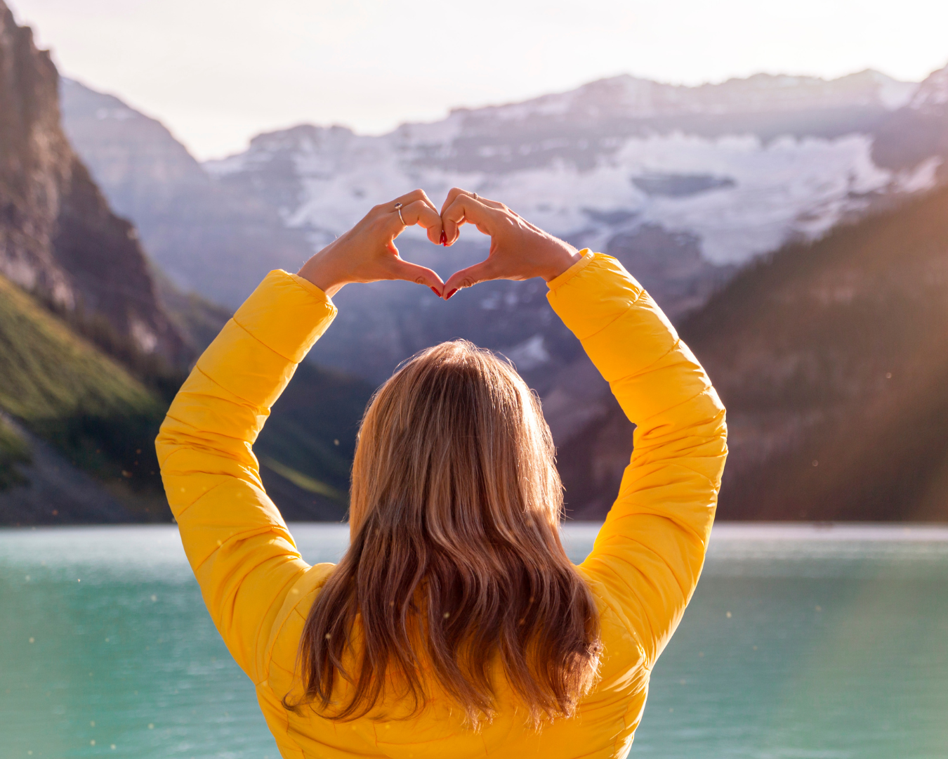 female back side, looking at lake with mountain, with hands over head, fingers in the shape of heart