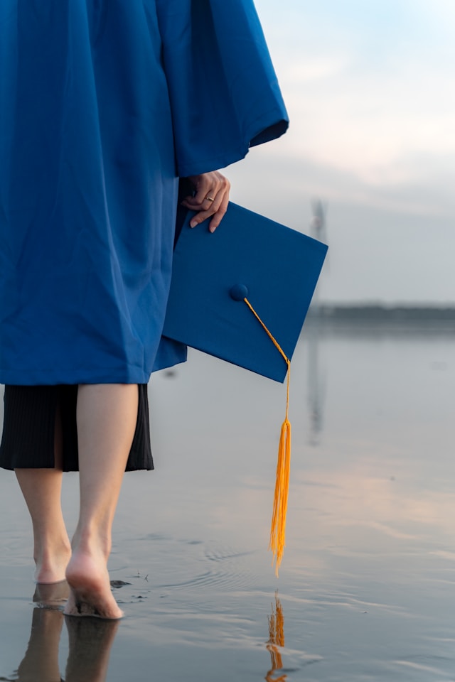 Young woman in a graduation cap and gown walking away through shallow water at sunset