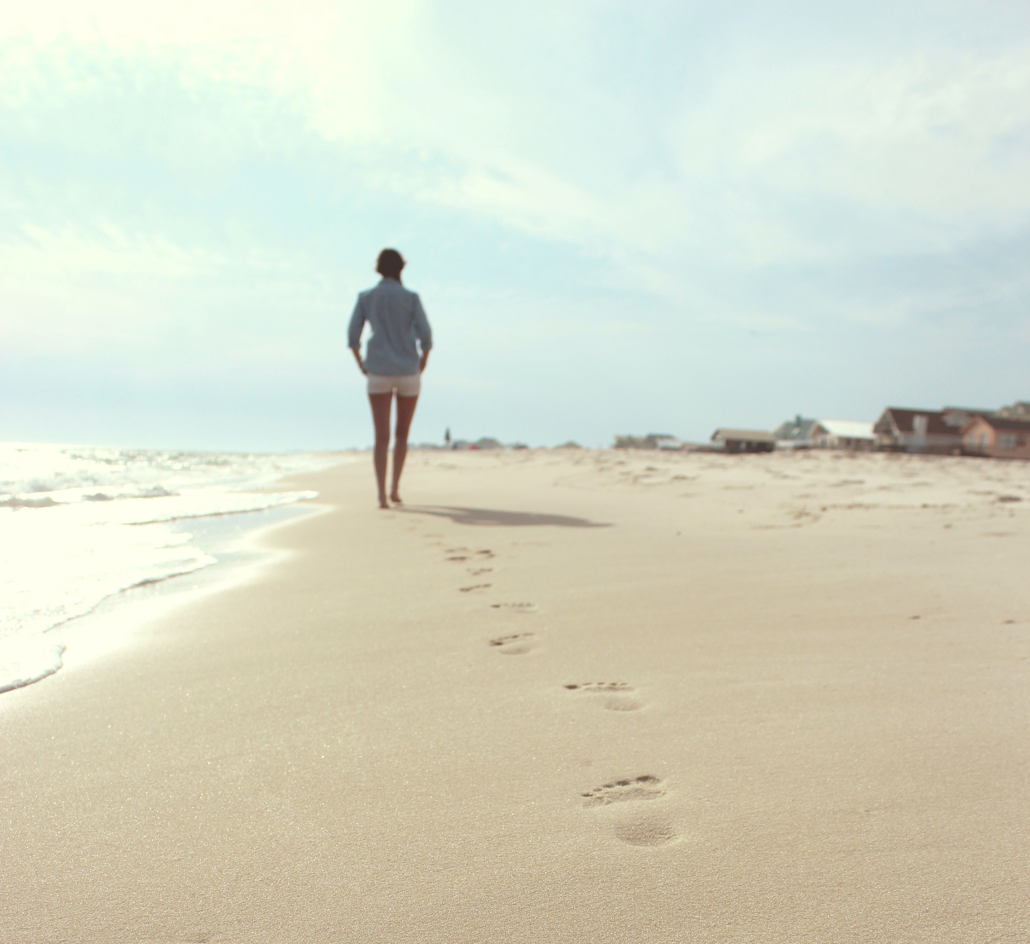 Woman-in-white shorts-walks-aways-on-beach-leaving-footsteps-in-the-white-sand