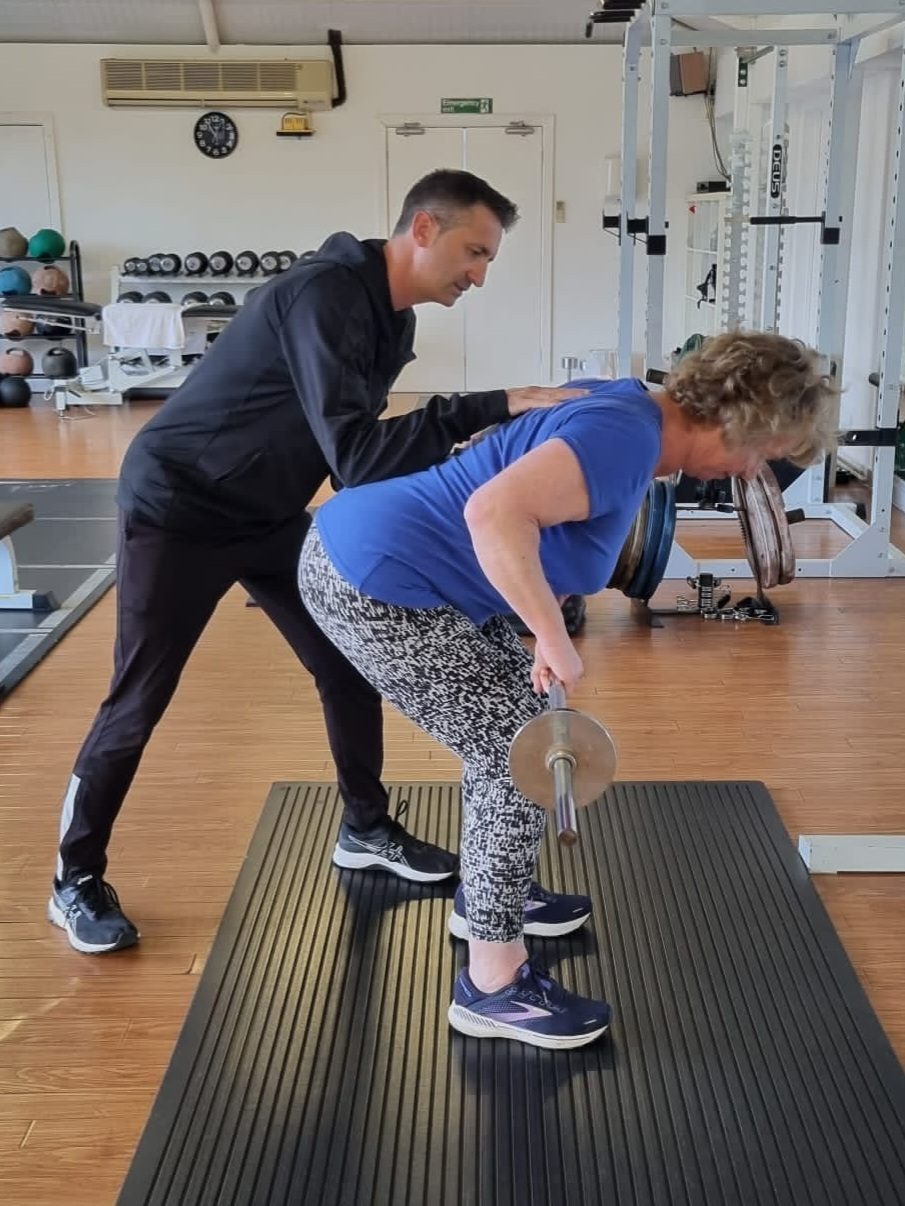 Personal trainer coaching a client through a bent-over row with a barbell