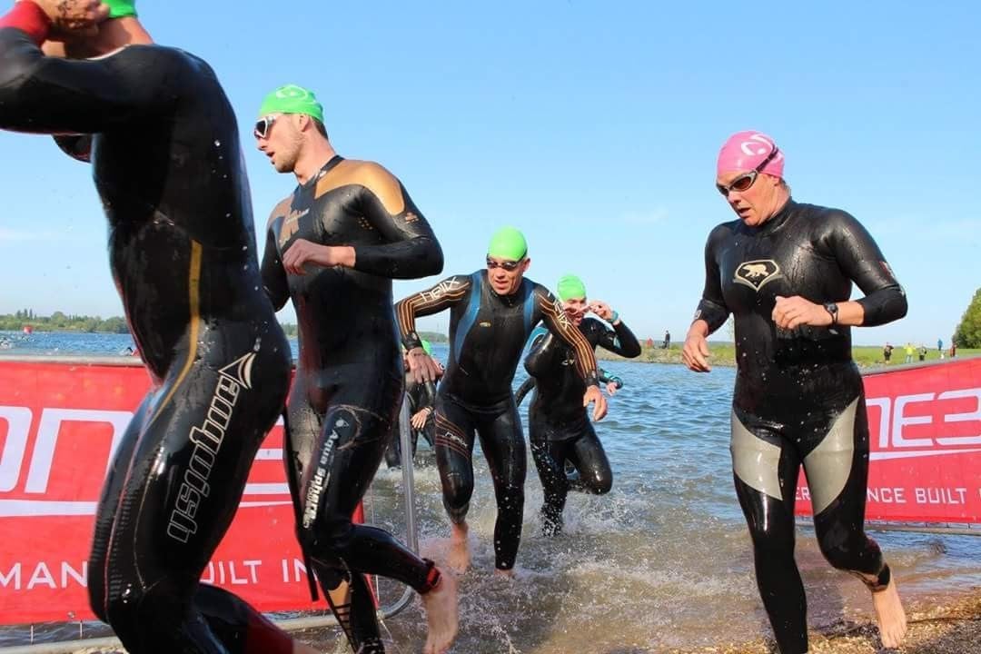 Triathletes in wetsuits running out of the water at the end of the swim