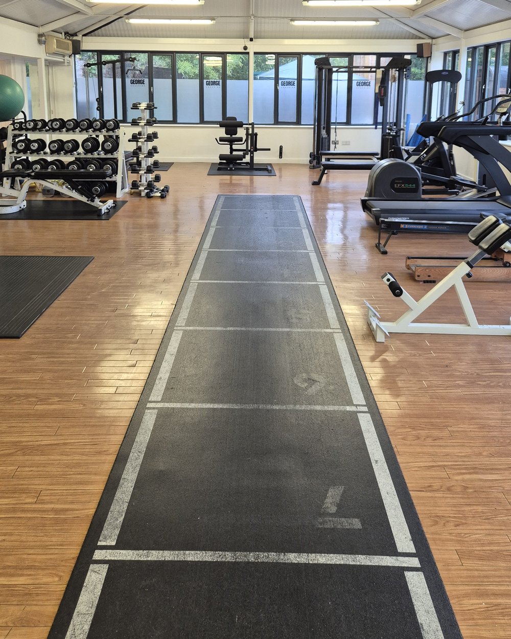 Open gym floor with dumbbell rack, benches and cardio equipment