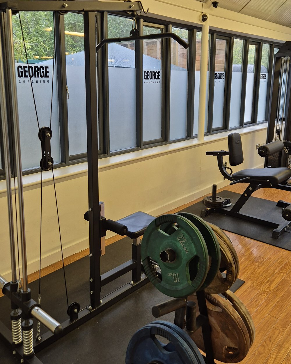 Cable machine and weight plates beside the George Coaching branded windows