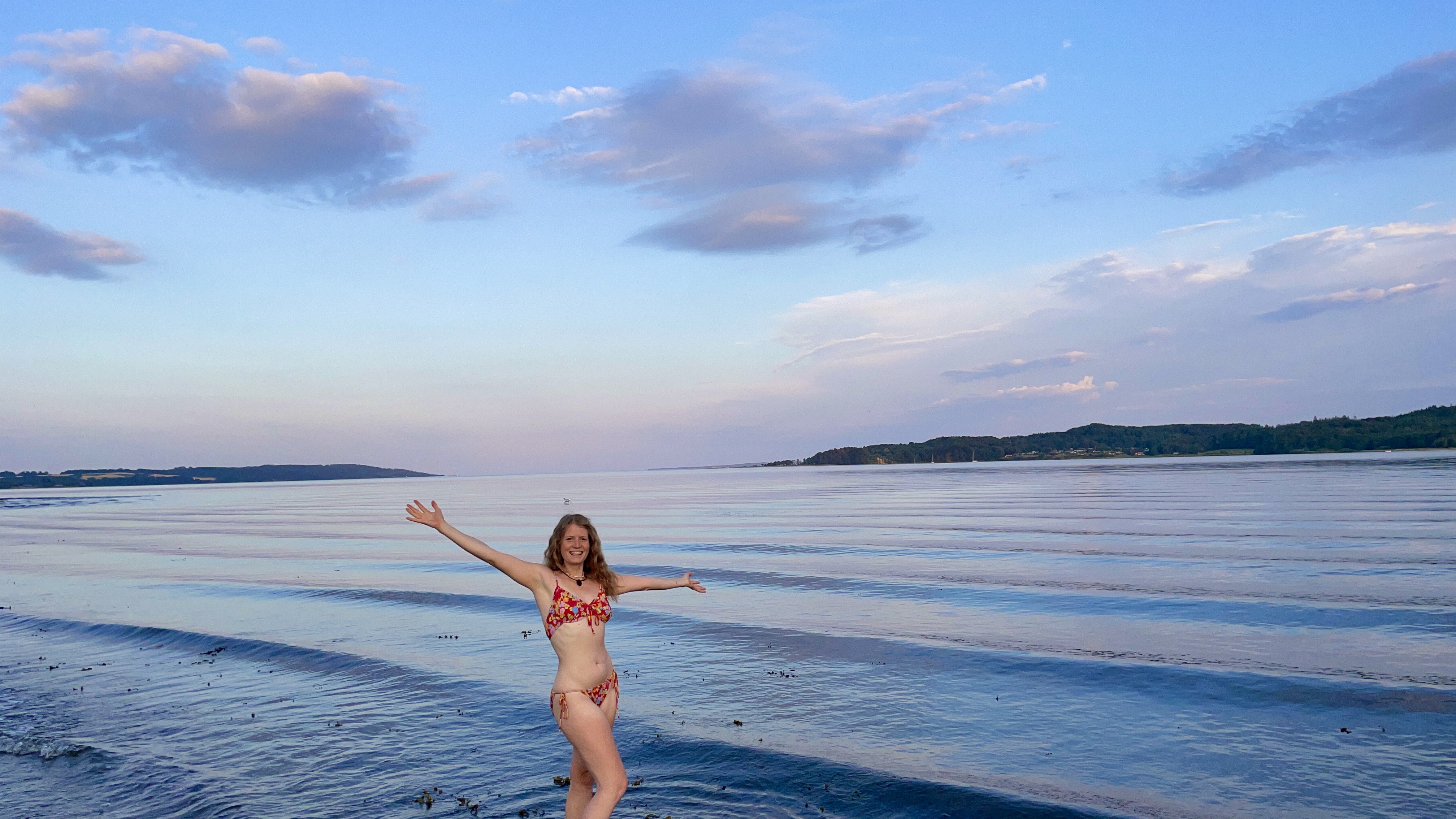 Julia at the shore at sunset with her arms open wide