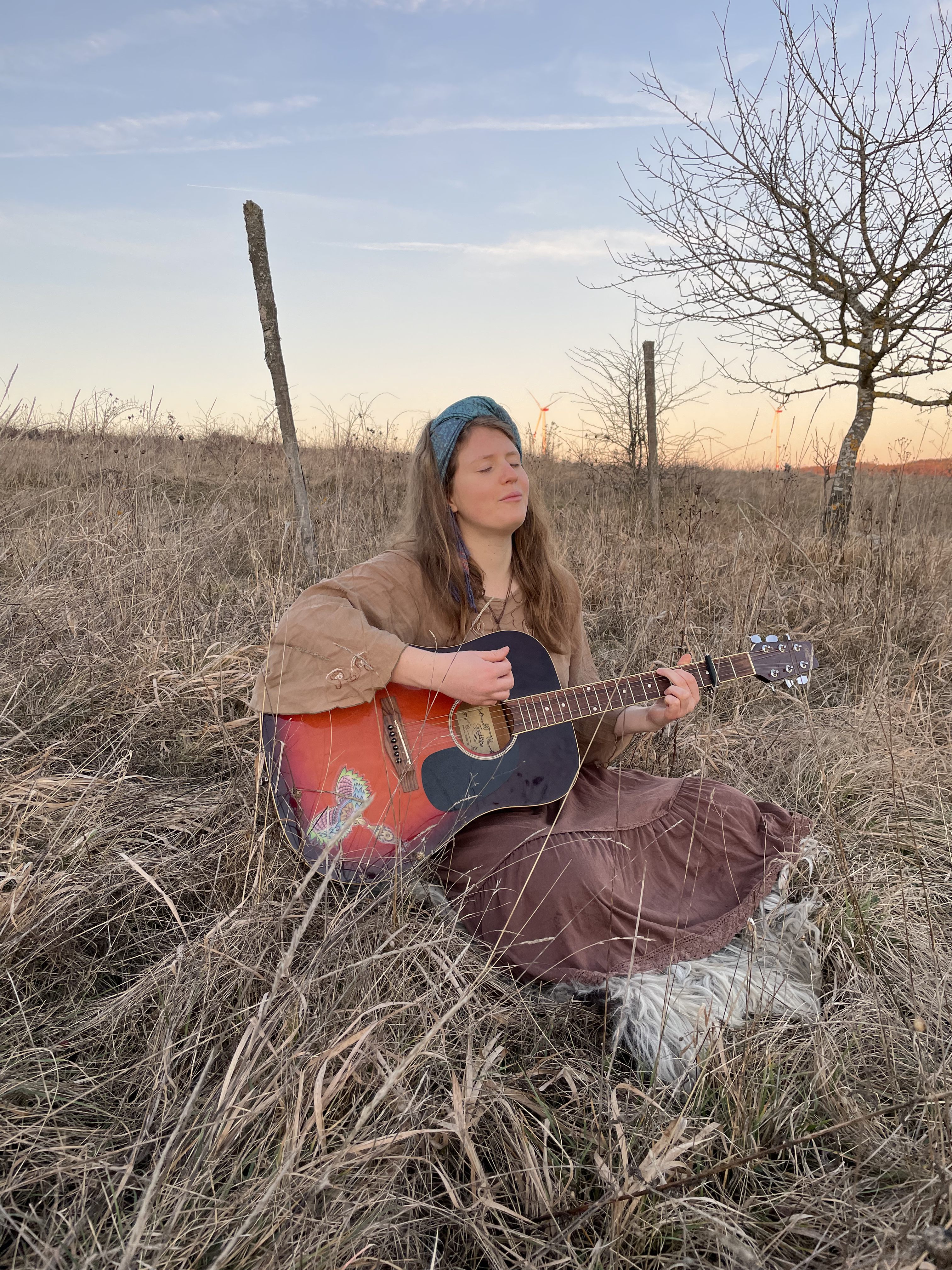 Julia Sana playing guitar in a field at sunset
