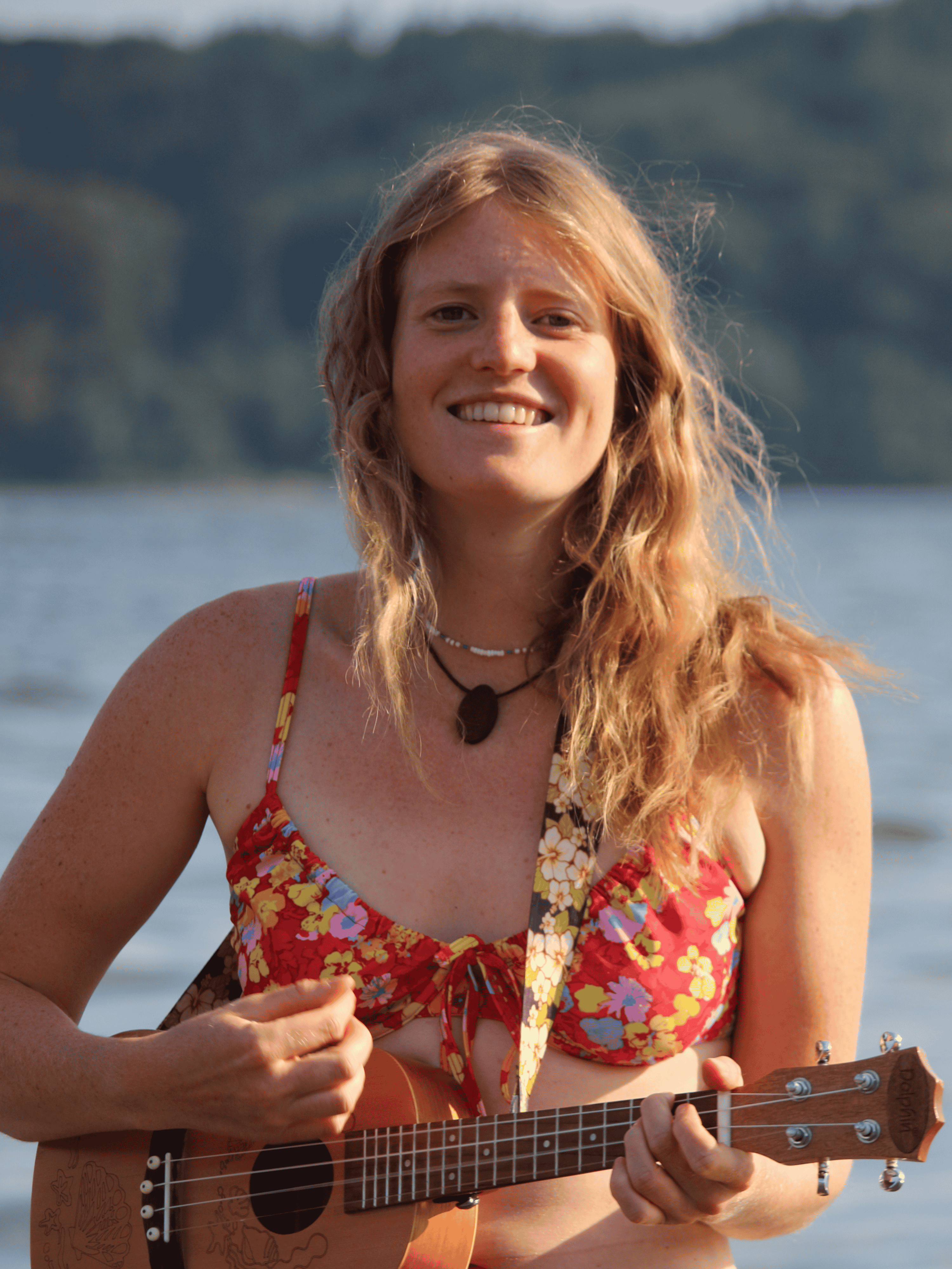 Julia Sana smiling with her ukulele by the water