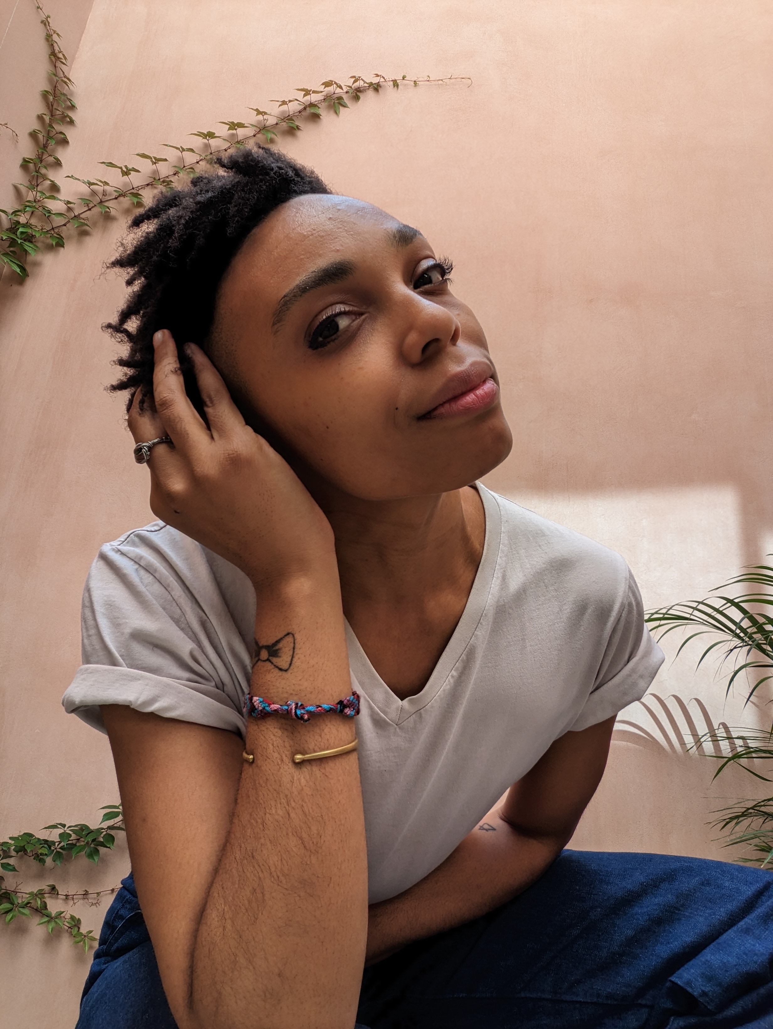 Photo of Isazela Amanzi (a Black person wearing a white t-shirt and blue jeans with short locs)