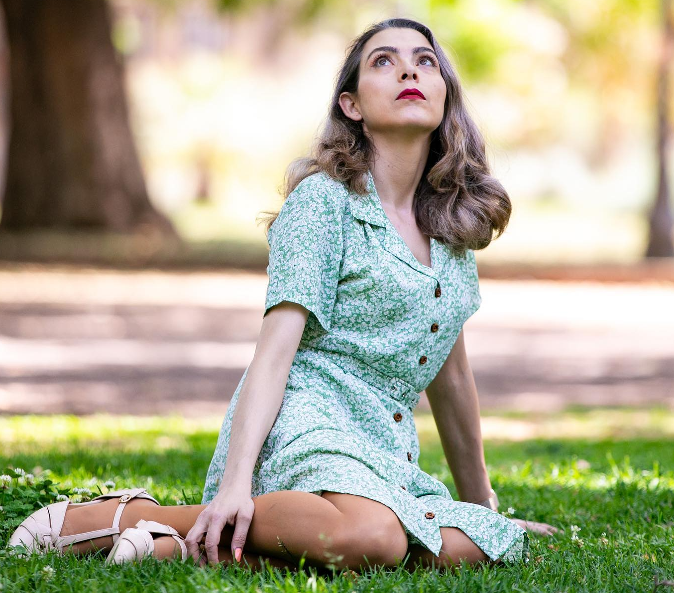 Emanuela seduta su un prato che guarda in alto, ha un vestitino azzurro a fiori bianchi