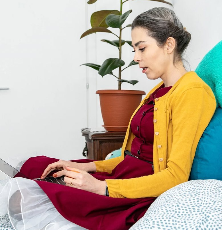 Foto di Emanuela Masia, è seduta con le gambe incrociate sul letto e scrive a computer, inquadratura di profilo