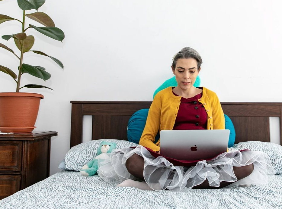 Foto di Emanuela seduta con le gambe incrociate a letto, sta scrivendo a computer