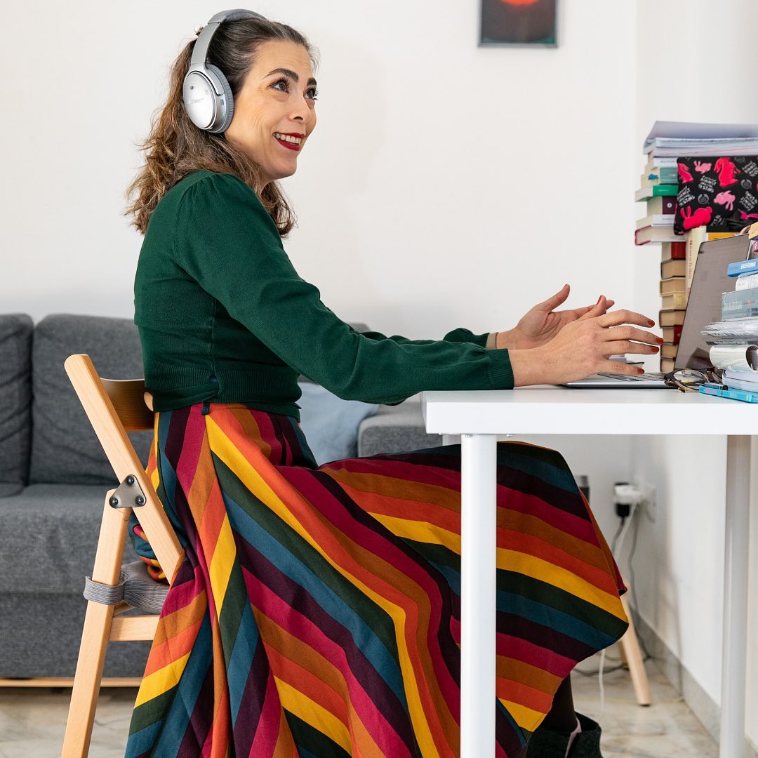 Emanuela seduta alla scrivania che scrive a computer, ha le cuffie e una gonna a strisce colorata