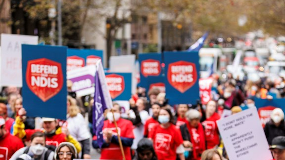 A photo from a previous Defend the NDIS rally. There are hundreds of people in the streets wearing EAC shirts and holding Defend the NDIS posters.