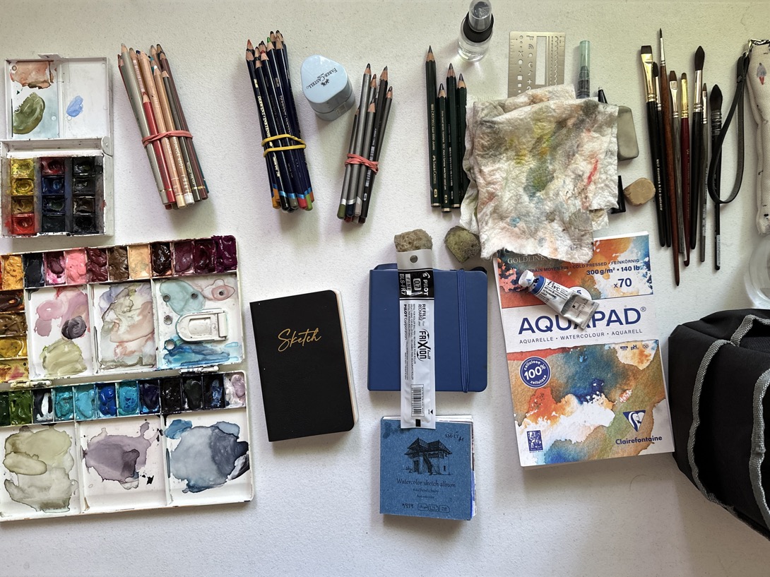 Photo depictiing an array of art materials including watercolours, colour pencils and brushes on a flatlay