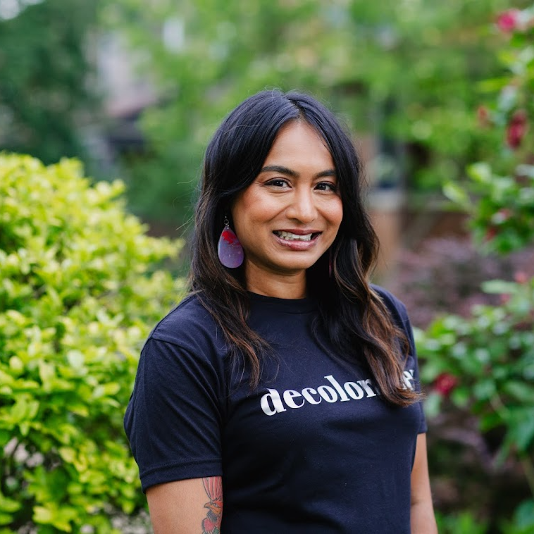 A woman wearing a decolonize tee shirt in front of some bushes