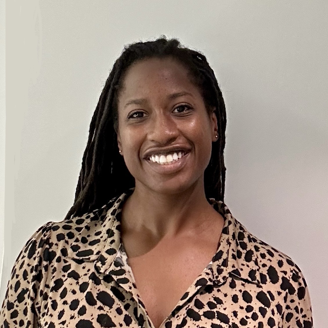 A woman wearing a tan with black splattered shirt in front of a gray wall