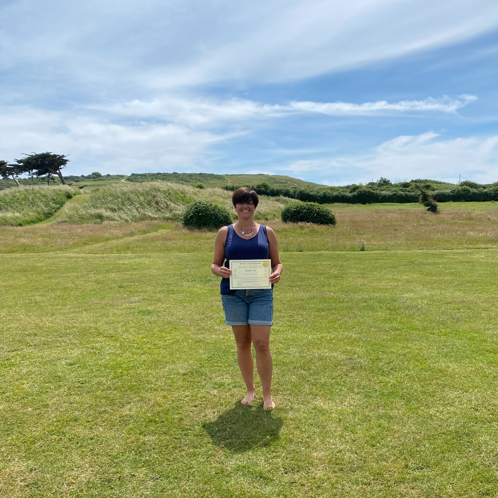 Reiki Master standing in a beautiful garden holding their Reiki Master certificate