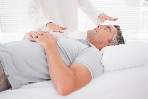 man lying on a reiki bed relaxing receiving hands off reiki from a reiki master