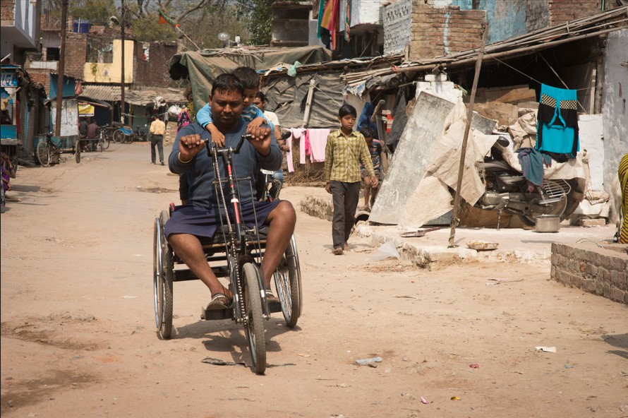 Amir Kumar Trike in India using a tricycle wheelchair with a little boy on his back