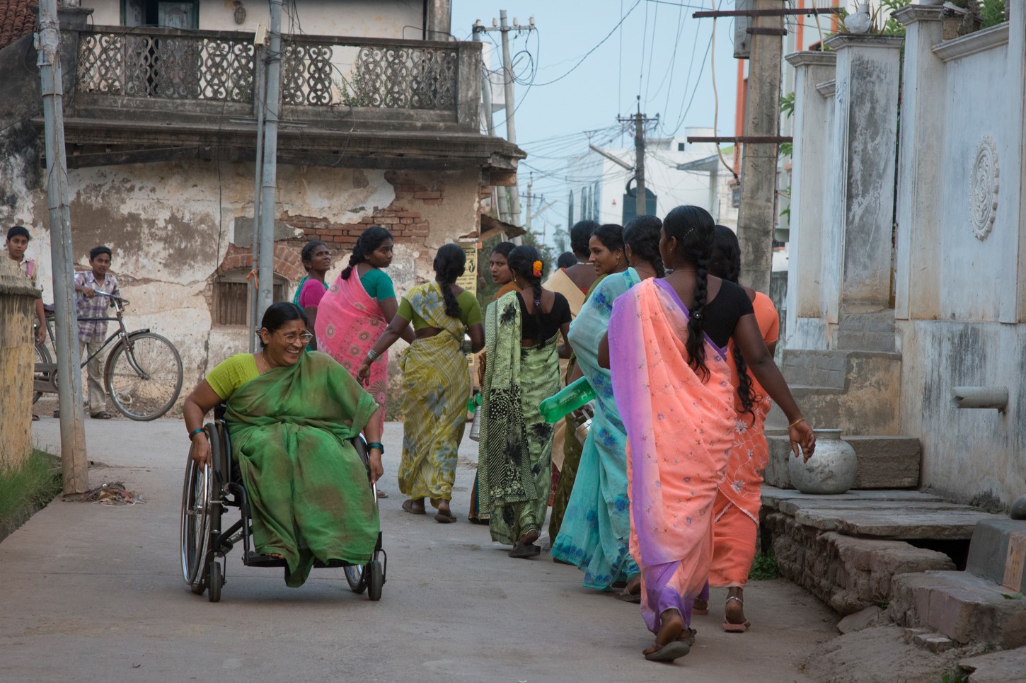 A smiling woman using a wheelchair rolling next to a group of women walking