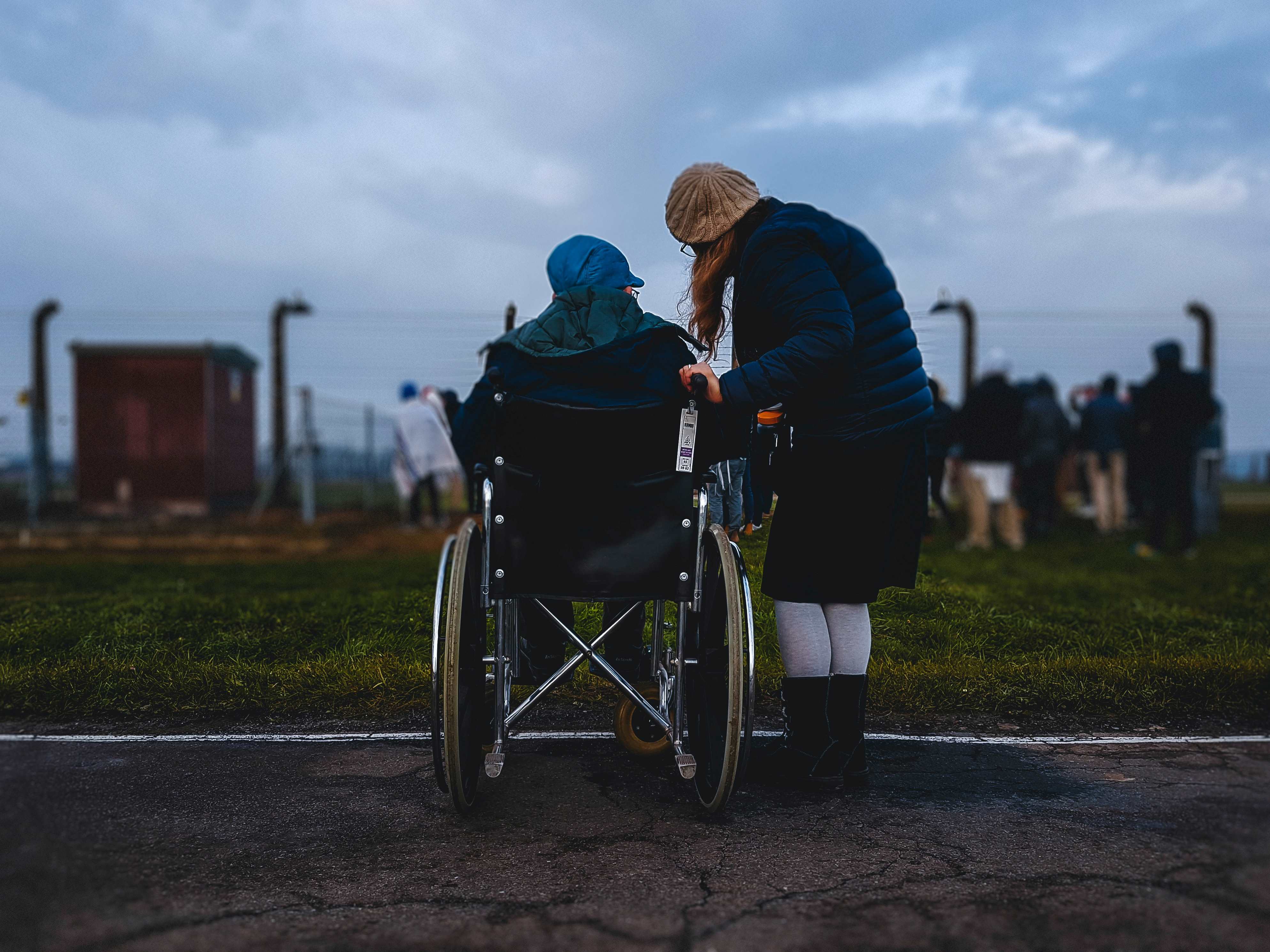 A woman in a wheelchair from her back with a woman beside her looking at the fence with people next to it