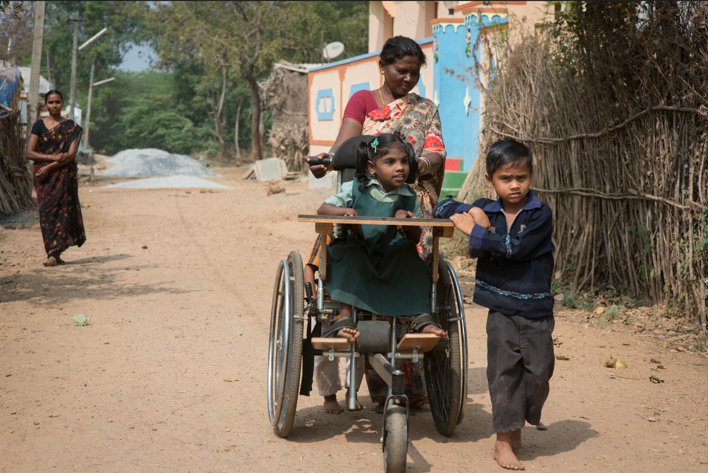 A mother and her son are pushing the wheelchair of their daughter/sister
