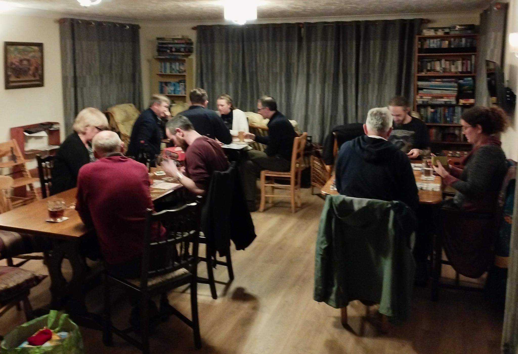 Lustleigh games club participant  seated in 3 groups of 3 or 4 participants playing board games in the guest lounge.  Alcoholic drinks on the tables.