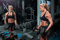 woman bodybuilder grabbing dumbells from dumbbell rack at the gym