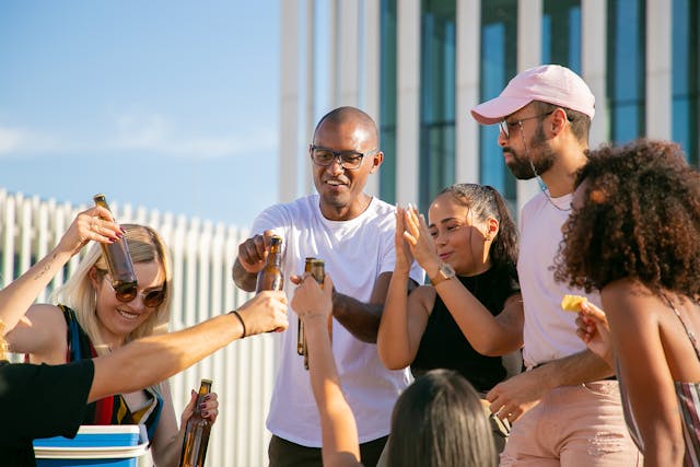 A multi-cultural group of people standing with drinks and food in hand celebrating and having fun, presented as the image for the Near Me Discovery blog content hub image for Food and Drink articles and posts, including best restaurants near me, best bars near me, best food to try near me, and best drinks near me