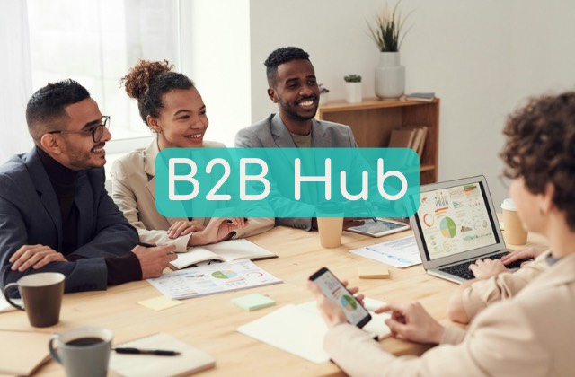 A cheerful multi-cultural group of business people dressed in business casual clothing in a professional setting sitting with phones, spreadsheets, business data, and presentations across the table as they strategize and collaborate, presented as the image for the Near Me Discovery blog content hub image for B2B articles and posts, including how to promote my local business, how to grow my small business, how to generate more brand awareness of my business near me, and how to increase customer retention and customer loyalty