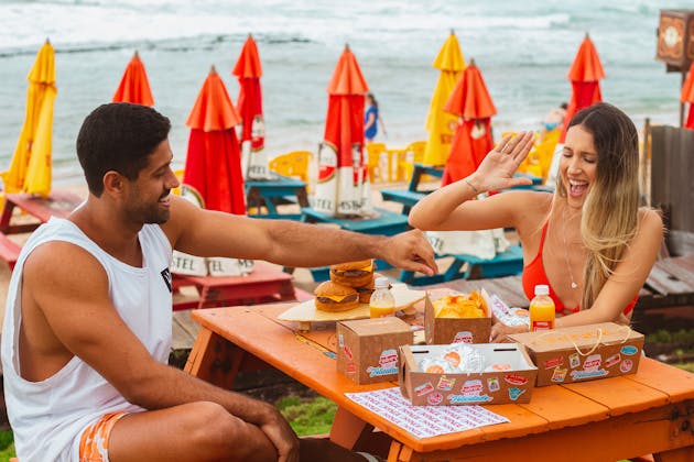 Picture of a man and woman sitting down to eat while laughing and having a great time at a restaurant that is beachside with a view of the beach waves in the image background, used as the blog post image for the article about the hidden gem restaurants loved by locals in Panama City Beach, FL for Near Me Discovery, local search and local discovery blog and advertising