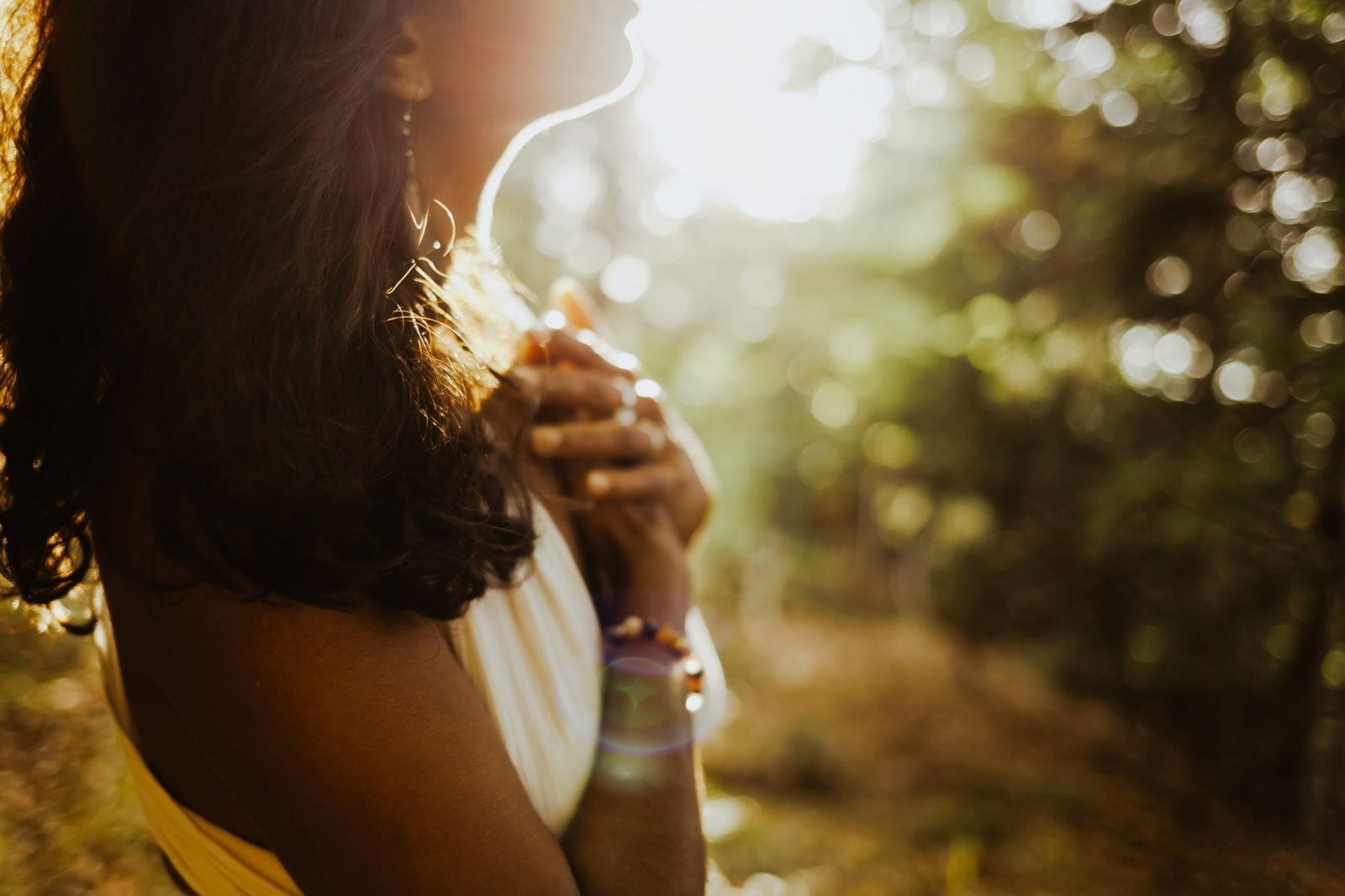 Davina de profil, les mains jointes sur le cœur, dans la lumière du soleil en forêt