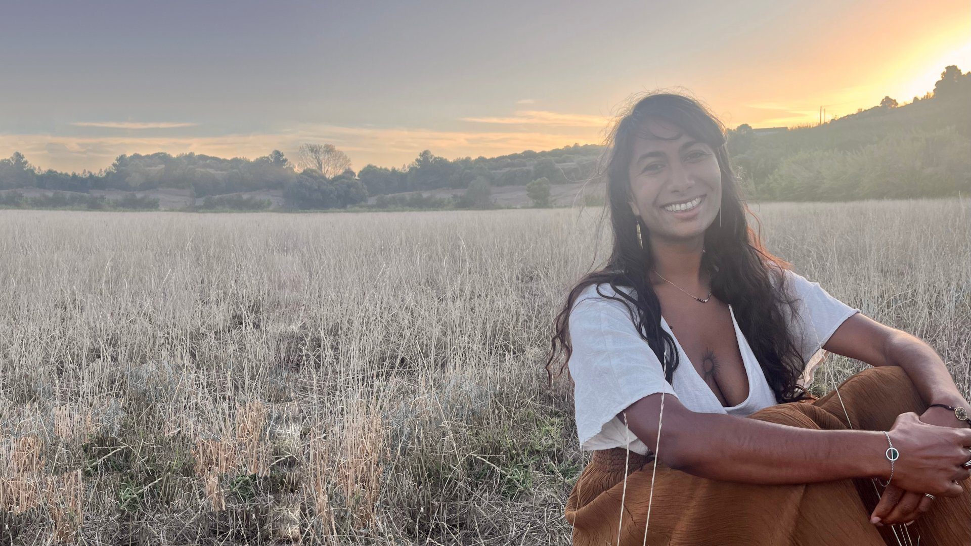 Davina souriante, assise dans un champ au coucher du soleil