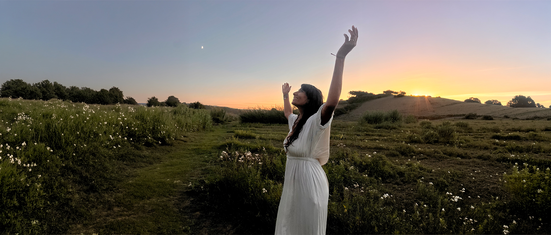 Davina, les bras levés vers le ciel au coucher du soleil, dans un champ fleuri