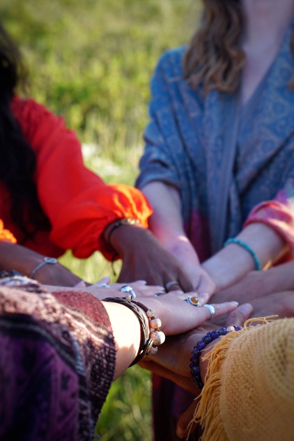 Des mains de femmes posées les unes sur les autres, au centre d’un cercle, dans l’herbe
