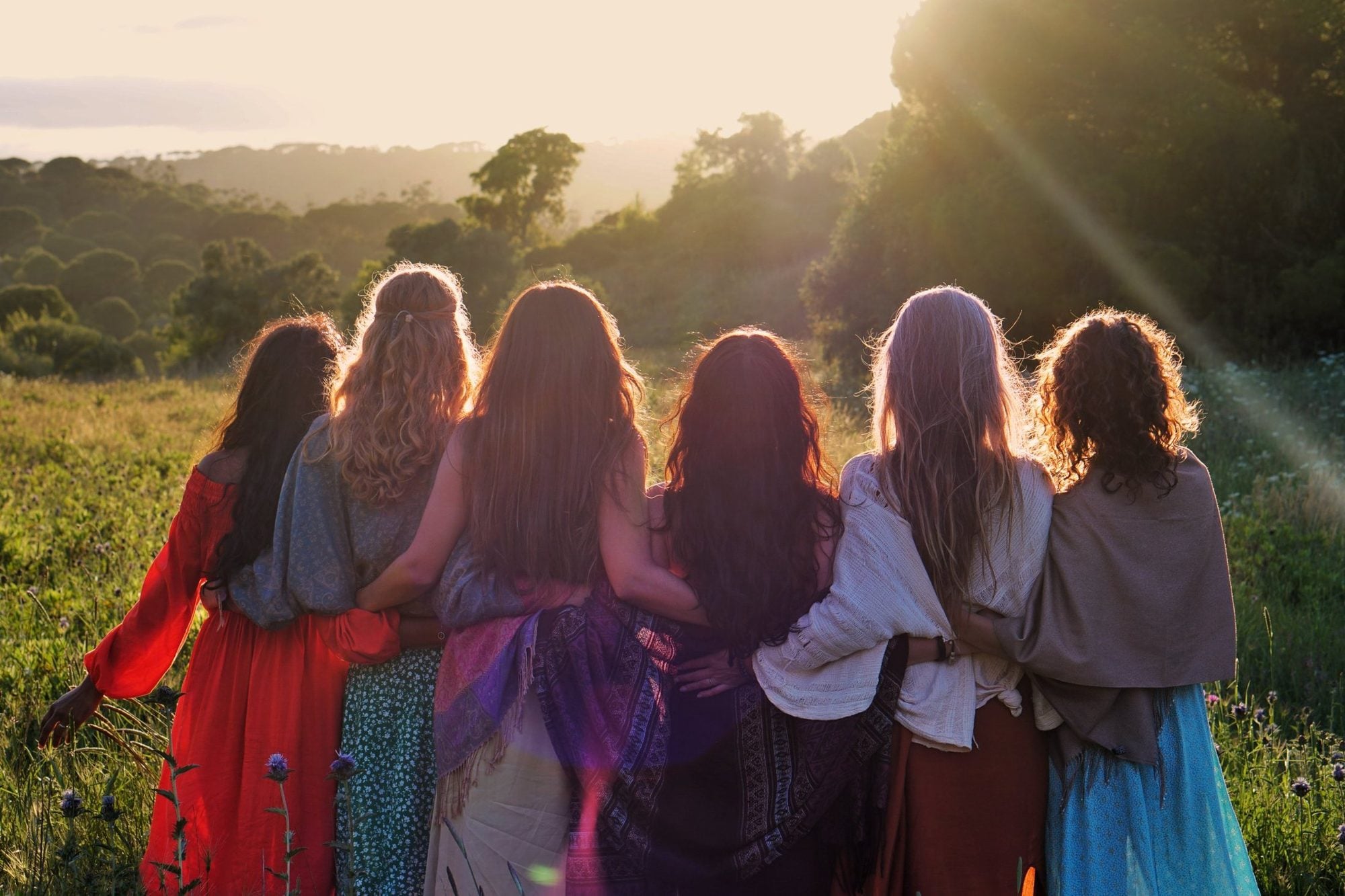 Six femmes enlacées, de dos, face au coucher de soleil