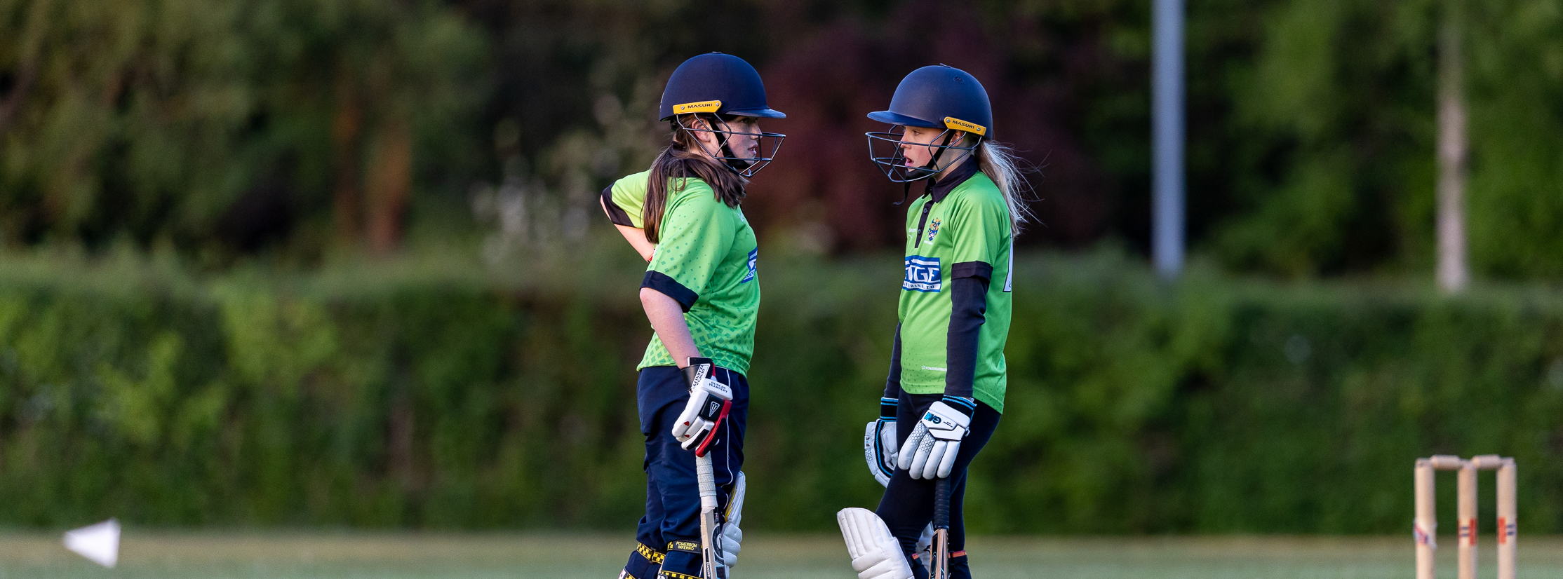 Junior girls bats people discussing tactics at the crease in between overs