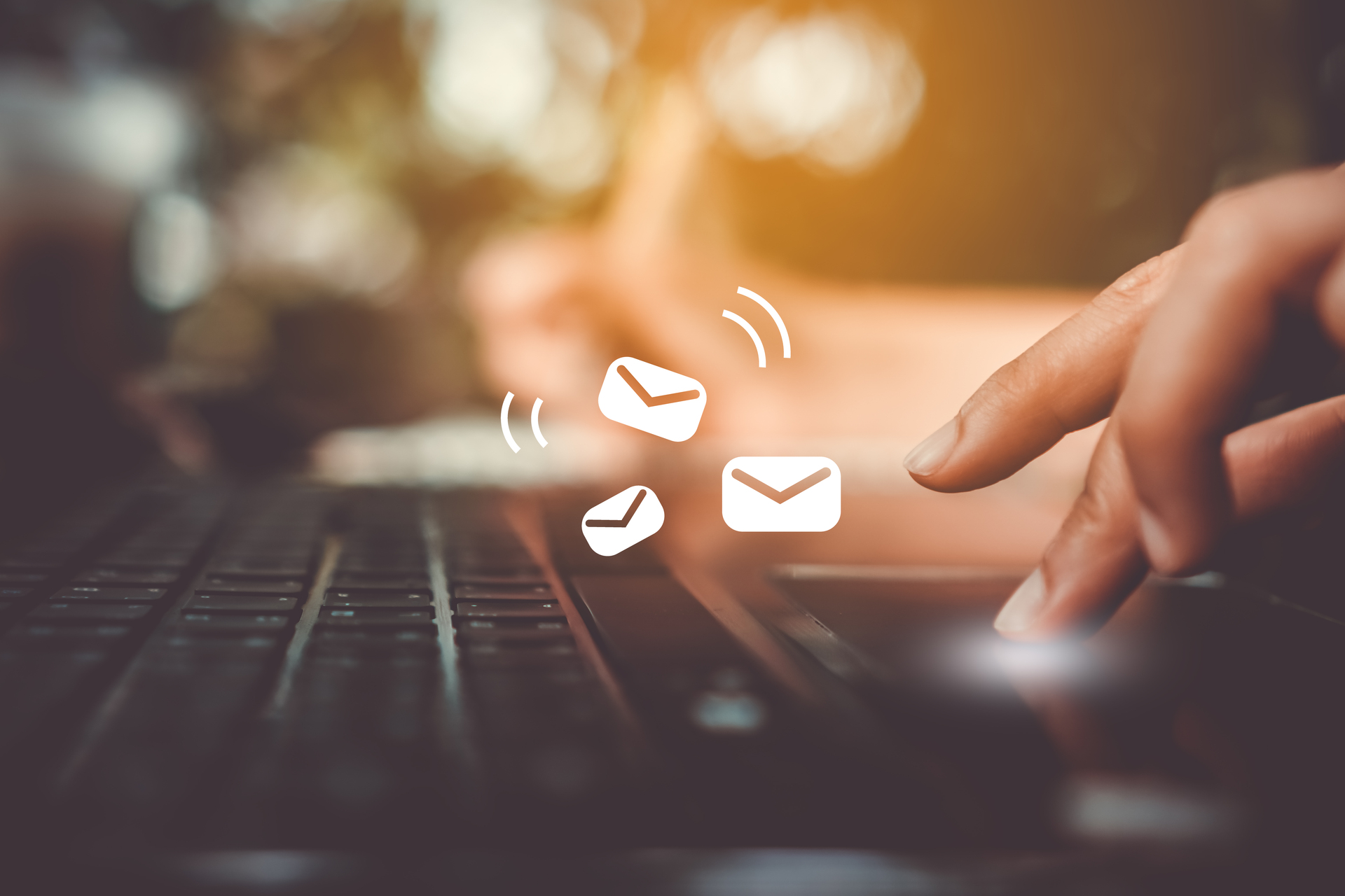 A hand typing on a keyboard with little envelopes signalling email floating over the keyboard.